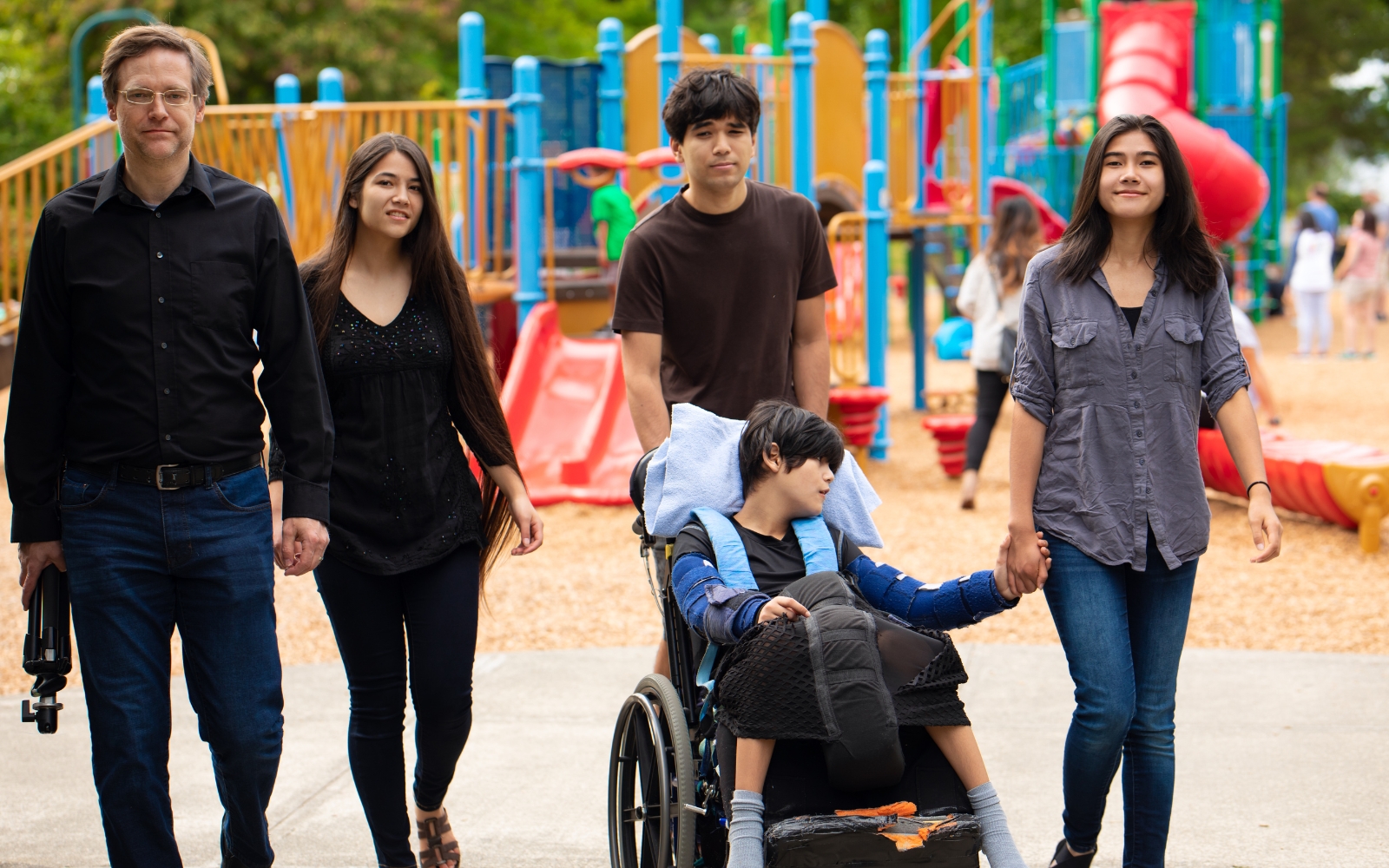 Child with disabilities in a wheel chair holding a woman's hand as she and the rest of the family walks away from a playground